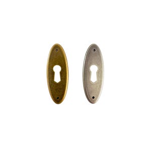 May include: Two antique-style keyhole covers. One is a brass color, the other is a silver color. Both are oval-shaped with a keyhole cutout in the center and two small screw holes. These are likely for furniture or door hardware.