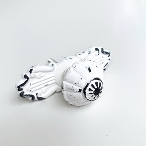 Könnte beinhalten: Weißer und schwarzer, verwitterter Metall-Schrankknauf mit einem dekorativen Blumenmuster.