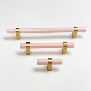 May include: Three pink cabinet knobs with gold metal accents. The knobs are in different sizes, with the largest being a 15cm pull.
