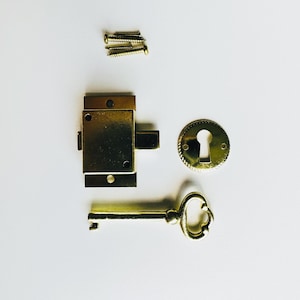 May include: A gold-toned keyhole cover, a brass key, and a brass lock with a latch. The lock has four screw holes. The keyhole cover has a decorative edge.