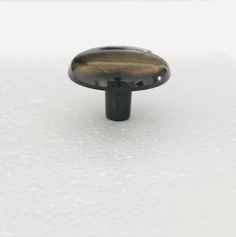 May include: A round, dark brown cabinet knob with a shiny finish. The knob has a short, black stem.