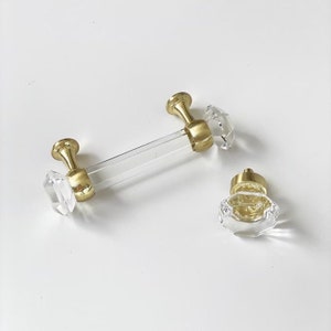 May include: Two gold and clear crystal cabinet knobs. One knob is a pull handle with a clear acrylic bar and crystal ends. The other knob is a round crystal knob.