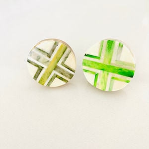 May include: Two round, white, decorative buttons with a green and gray geometric pattern. The buttons have a raised, circular design.