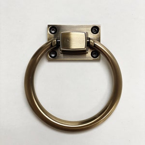 Pode incluir: Uma pega de puxar em anel de latão com uma placa traseira quadrada. A pega é fixada à placa traseira com quatro parafusos.