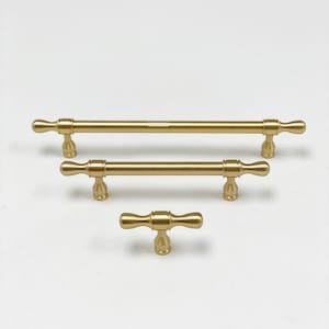 May include: Three brass-colored cabinet pulls in varying sizes are arranged on a white background. The pulls have a T-bar design with rounded ends and a matte finish. The largest pull is approximately 12 inches long, the medium pull is 6 inches, and the smallest is 3 inches.