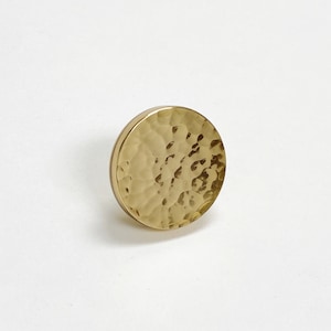 May include: A round, hammered gold-toned metal knob. The knob has a textured surface and a smooth, flat back.