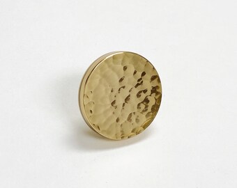 May include: A round, hammered gold-toned metal knob. The knob has a textured surface and a smooth, flat back.