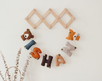 May include: A felt letter banner spelling "ISHA" with a brown bear and a fox at either end. The banner is hanging on a wooden wall rack.