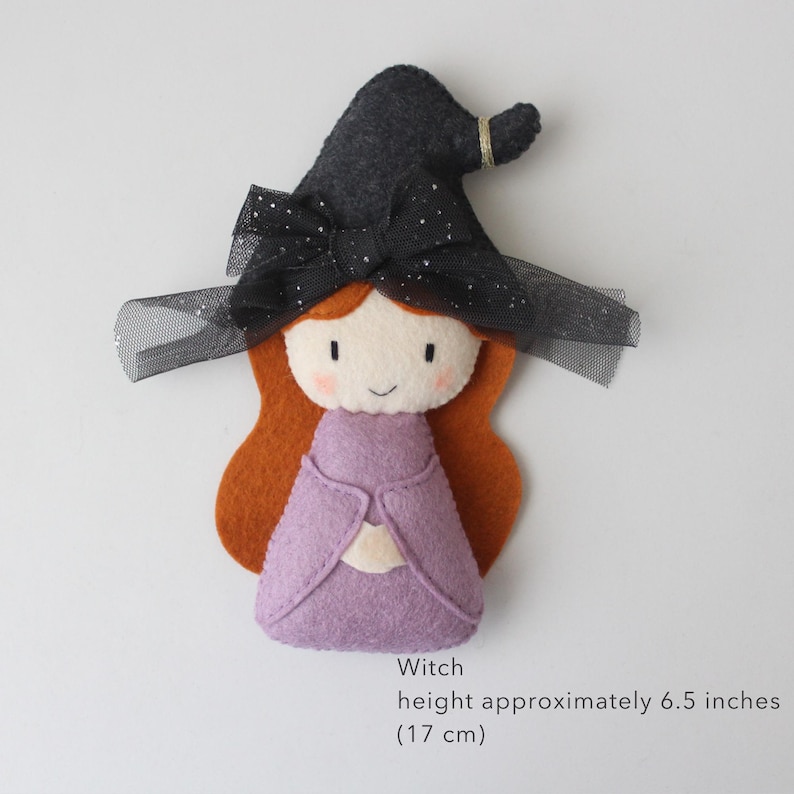 May include: A felt witch doll with a black hat, orange hair, and a purple dress. The witch doll is approximately 6.5 inches (17 cm) tall. The hat has a black bow and gold trim. A cute Halloween decoration.