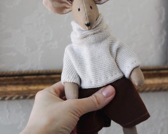May include: A handmade plush deer doll with brown antlers, tan ears, and a beige face. The deer wears a white knit sweater and brown shorts. A charming, whimsical stuffed animal.