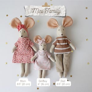 May include: Three handmade mouse dolls, labeled "Mom," "Girl/Boy," and "Dad," stand against a white background with gold star accents. The dolls are dressed in fabric outfits, with the "Mom" and "Girl/Boy" dolls wearing dresses and the "Dad" doll in a shirt and pants. The "Mom" and "Dad" dolls are 8.5 inches (22 cm) tall, and the "Girl/Boy" doll is 6 inches (16 cm) tall. The text "Mini Family" is above the dolls.