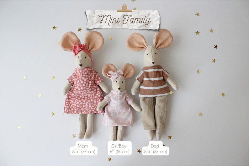 May include: Three handmade mouse dolls, labeled "Mom," "Girl/Boy," and "Dad," stand against a white background with gold star accents. The dolls are dressed in fabric outfits, with the "Mom" and "Girl/Boy" dolls wearing dresses and the "Dad" doll in a shirt and pants. The "Mom" and "Dad" dolls are 8.5 inches (22 cm) tall, and the "Girl/Boy" doll is 6 inches (16 cm) tall. The text "Mini Family" is above the dolls.