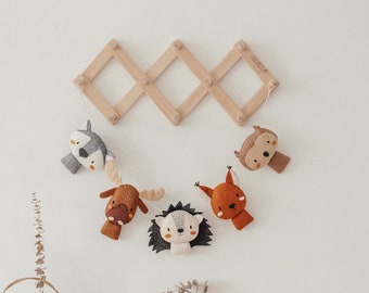 May include: A wooden wall-mounted rack with five felt animal heads hanging from it. The animals are a wolf, a moose, a hedgehog, a squirrel, and an owl. The rack is in a diamond pattern and has a light wood finish.