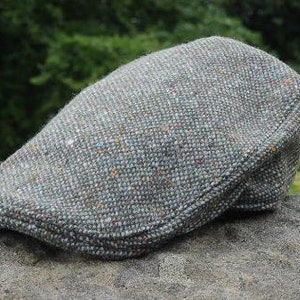 Puede incluir: Una gorra plana de tweed gris con un patrón texturizado. La gorra tiene una visera ligeramente curvada y una corona puntiaguda.