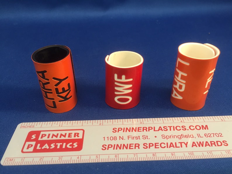 May include: Three red plastic award cylinders with white and black lettering. The cylinders are labeled "LHRA KEY", "OWF", and "LHRA".