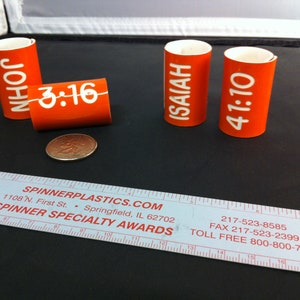 May include: Four orange plastic tubes with white text. The tubes have the following text: "JOHN 3:16", "ISAIAH", and "41:10".