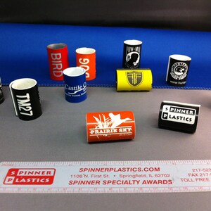 May include: Assortment of colorful, cylindrical promotional products with various logos and text.  The products are made of plastic and have a diameter of approximately 2 inches.  The text on the products includes "Bird", "90", "Castile", "TM27", "Mayhe Mu", "Prairie Sky", "Spinner Plastics", "RWW", "www.hun", and "Twin-Mix".