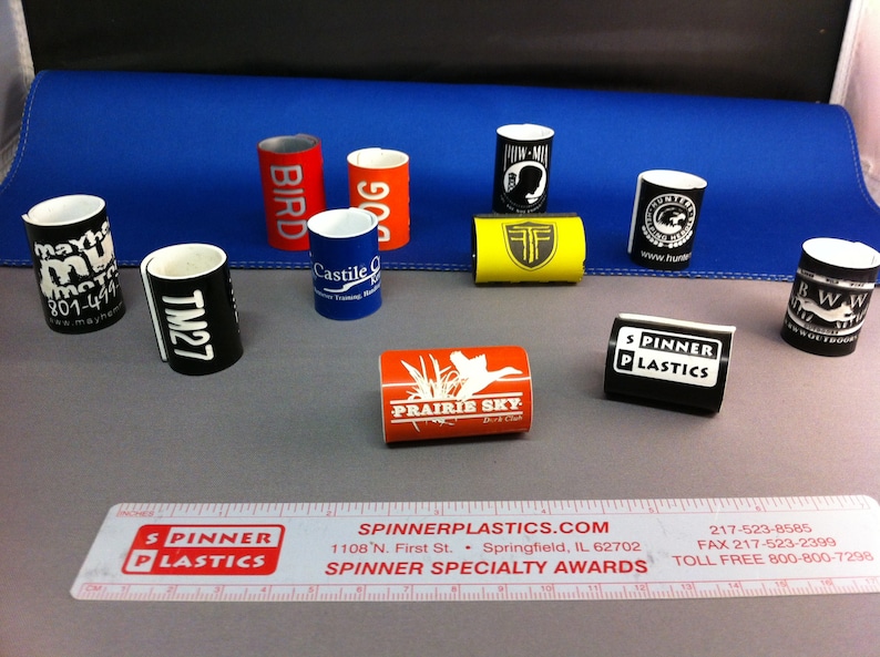 May include: Assortment of colorful, cylindrical promotional products with various logos and text.  The products are made of plastic and have a diameter of approximately 2 inches.  The text on the products includes "Bird", "90", "Castile", "TM27", "Mayhe Mu", "Prairie Sky", "Spinner Plastics", "RWW", "www.hun", and "Twin-Mix".