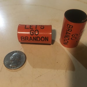 May include: Two orange foam bracelets with black text. The text on one bracelet reads "Let's Go Brandon" and the other reads "Go Brandon".