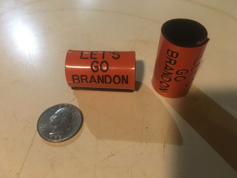 May include: Two orange foam bracelets with black text. The text on one bracelet reads "Let's Go Brandon" and the other reads "Go Brandon".