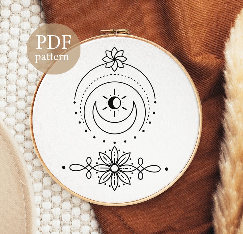May include: A black and white embroidery pattern featuring a crescent moon, sun, and two stylised flowers. The pattern is displayed on a white embroidery hoop.
