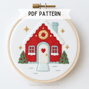 Puede incluir: Arte de aro bordado con una casa roja con detalles blancos, una puerta en forma de corazón y dos árboles de Navidad verdes. El diseño incluye el texto "PDF PATTERN" y está sobre un fondo blanco. El bordado está en un aro de madera.