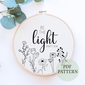 May include: Black and white embroidery pattern for a hoop art project. The design features the text "Be the light" with the Bible verse "Matt 5:14" and a floral design.