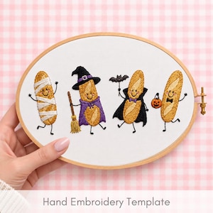 May include: An oval wooden embroidery hoop containing white fabric with hand-stitched baguette characters dressed for Halloween. The designs include a mummy, a witch with a broom, a vampire with a bat, and a baguette holding a pumpkin bucket.