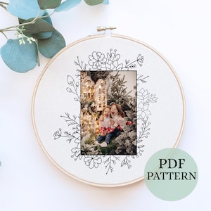 May include: A black and white embroidery pattern of a Christmas scene with two children standing in front of a decorated Christmas tree. The pattern is framed in a hoop and includes a floral border.
