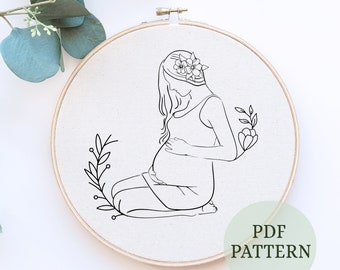 May include: Line art embroidery pattern of a pregnant woman holding her belly, with flowers in her hair and a floral design on the side. The pattern is on a white background and says "PDF PATTERN" at the bottom.