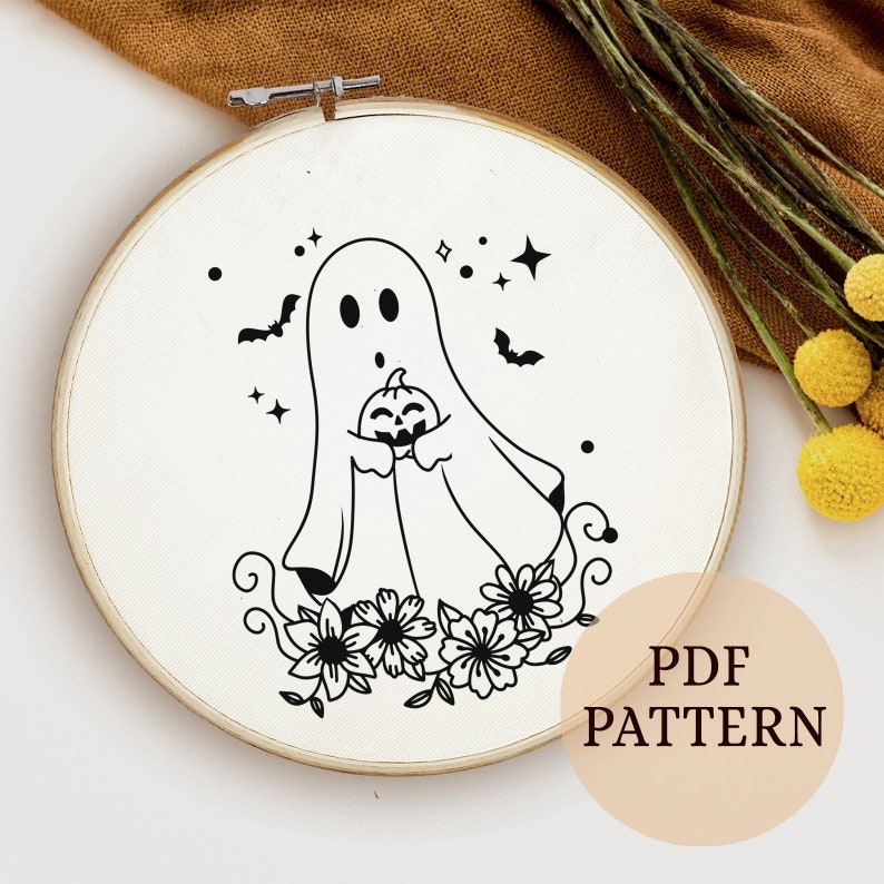 Peut inclure: Un motif de broderie en noir et blanc d'un fant&ocirc;me tenant une citrouille avec des fleurs en bas. Le motif est sur un fond blanc et se trouve dans un cercle de broderie rond. Le texte "PDF PATTERN" est dans le coin inf&eacute;rieur droit de l'image.