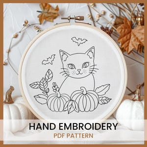 May include: Black and white line art embroidery pattern of a cat sitting with pumpkins and leaves. The pattern is in a round embroidery hoop. The text "HAND EMBROIDERY PDF PATTERN" is below the hoop.