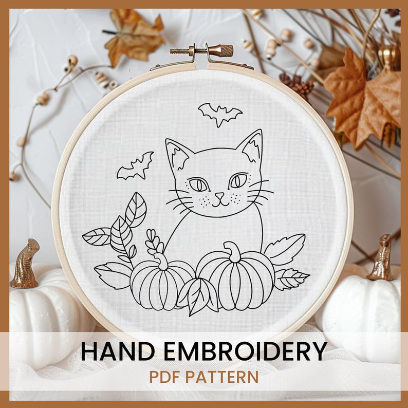 May include: Black and white line art embroidery pattern of a cat sitting with pumpkins and leaves. The pattern is in a round embroidery hoop. The text "HAND EMBROIDERY PDF PATTERN" is below the hoop.