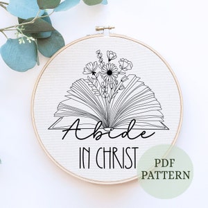 May include: Black and white embroidery pattern featuring an open book with flowers and the text "Abide in Christ".