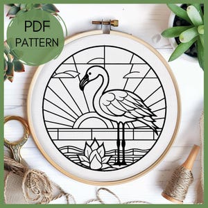 May include: Black and white line art embroidery pattern of a flamingo standing in water with a sunrise behind it. The pattern is in a circular hoop.
