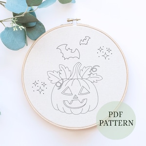May include: Black and white line art embroidery pattern of a jack-o'-lantern with leaves, bats, and stars. The pattern is on a white fabric in a round embroidery hoop. The text "PDF PATTERN" is at the bottom of the image.