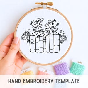 May include: A hand embroidery template featuring a line drawing of books and flowers. The design is in a wooden embroidery hoop. The text "HAND EMBROIDERY TEMPLATE" is at the bottom. Several spools of DMC embroidery floss are below the hoop.