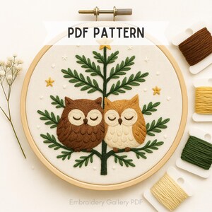 May include: A circular embroidery hoop with a design of two owls on a tree. The owls are brown and beige, with closed eyes, set against a cream background. The design includes green leaves, yellow stars, and the text "PDF PATTERN".