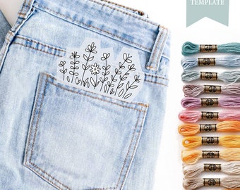 May include: A close-up of a pair of blue jeans with a pocket that has a floral embroidery design on it. The design is outlined in black and includes a flower and leaves. There are 12 spools of embroidery floss in various colors to the right of the jeans.