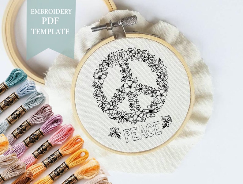 May include: A black and white embroidery pattern of a peace sign surrounded by flowers. The pattern is on a white fabric in a wooden embroidery hoop. The text "PEACE" is below the peace sign. There are multiple spools of embroidery floss in various colors.