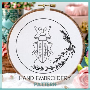 Peut inclure: Motif de broderie &agrave; la main en noir et blanc repr&eacute;sentant un scarab&eacute;e stylis&eacute; avec des d&eacute;tails floraux. Le motif est pr&eacute;sent&eacute; dans un cerceau de broderie en bois. "HAND EMBROIDERY PATTERN" est &eacute;crit en noir sous le cerceau.