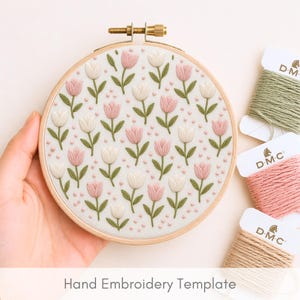 Op de afbeelding: Een borduurring met een bloemenpatroon van roze en witte tulpen en groene bladeren. De ring wordt in een hand gehouden. DMC borduurgaren in groen, roze en beige staan op de achtergrond. De tekst "Hand Embroidery Template" staat onderaan.