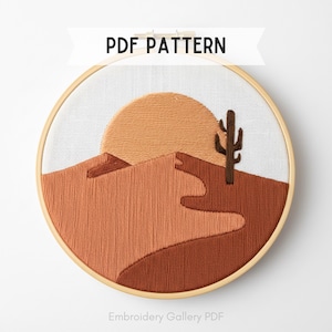 May include: An embroidery hoop featuring a desert landscape design. The artwork includes a sun, mountains, and a cactus, all rendered in shades of orange and brown thread. The text "PDF PATTERN" is displayed at the top, with "Embroidery Gallery PDF" at the bottom.