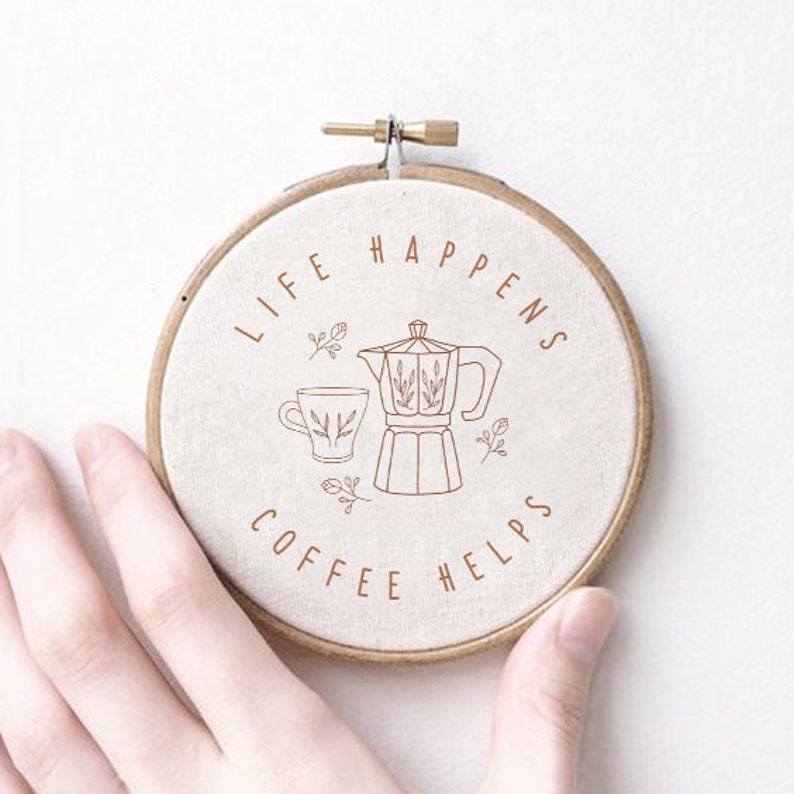 May include: A white embroidery hoop with the text "Life Happens Coffee Helps" and a line drawing of a coffee pot and a cup of coffee.