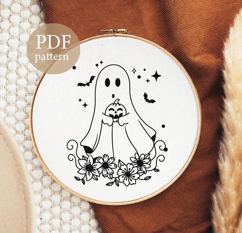 Peut inclure: Motif de broderie noir et blanc d'un fant&ocirc;me tenant une citrouille avec des fleurs et des &eacute;toiles autour. Le motif est sur un fond blanc et se trouve dans un cerceau de broderie rond.