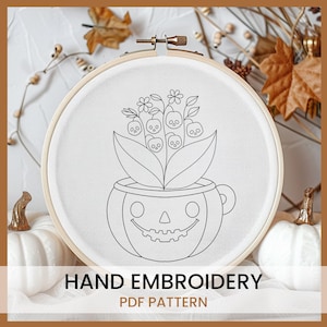 May include: A black and white line drawing of a pumpkin with a smiling face and a bouquet of flowers with skulls in the center. The image is in a hoop and is labeled "HAND EMBROIDERY PDF PATTERN".