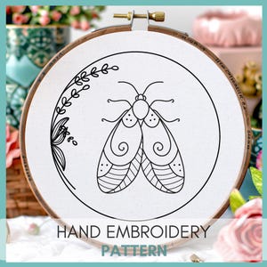 Peut inclure: Motif de broderie &agrave; la main en noir et blanc d'un papillon de nuit avec des d&eacute;tails complexes sur ses ailes. Le motif est affich&eacute; sur un tissu blanc tendu dans un cerceau de broderie en bois. Le texte "HAND EMBROIDERY PATTERN" est imprim&eacute; sous le cerceau.