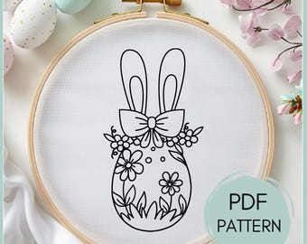 Op de afbeelding: Zwart-witte lijntekening borduurpatroon van een paasei met konijnenoren en een strik, omringd door bloemen en bladeren. Het patroon is op een witte stoffen achtergrond en is gelabeld "PDF PATTERN".