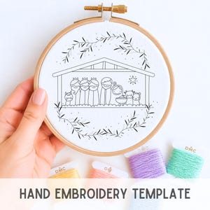 May include: A hand holding an embroidery hoop with a black and white line drawing of a nativity scene. The design is surrounded by a leafy wreath. Below the hoop are spools of colorful embroidery floss, and the text "HAND EMBROIDERY TEMPLATE".