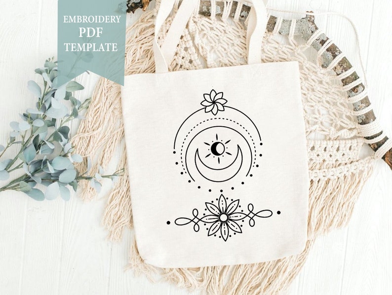 May include: A white tote bag featuring a black embroidered design of a sun, moon, and flower. The embroidery design is minimalist in style. The text "EMBROIDERY PDF TEMPLATE" is on a blue background.